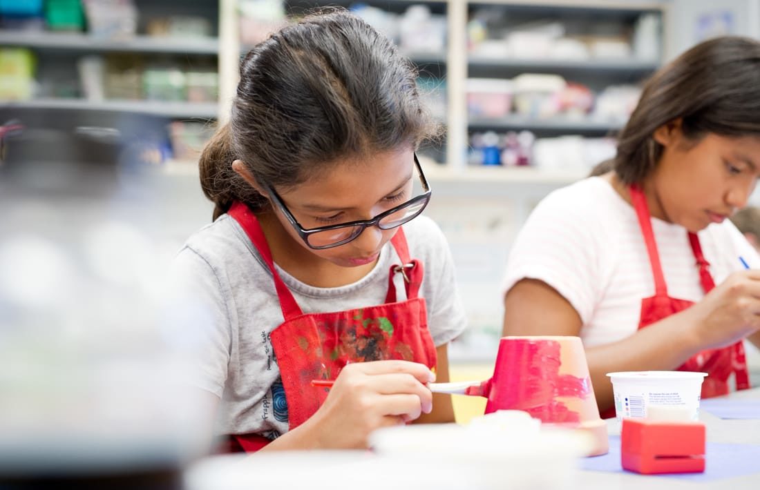 Two girls wearing red smocks and painting