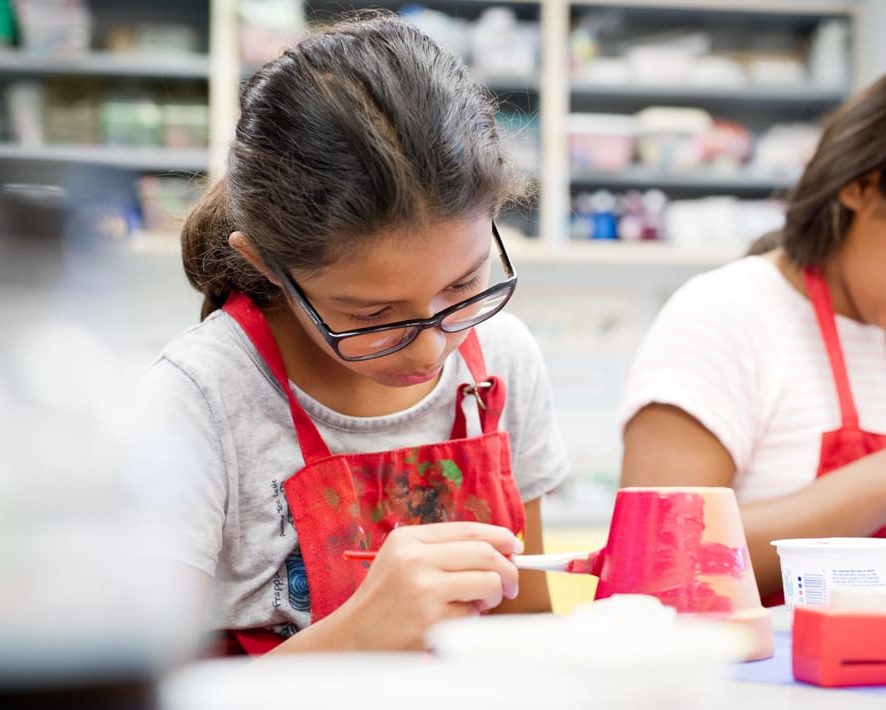 Two girls wearing red smocks and painting