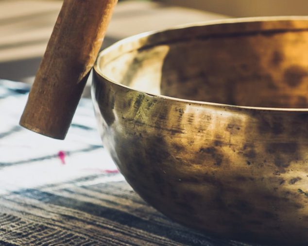 A hand using a stick to hit a sound bowl