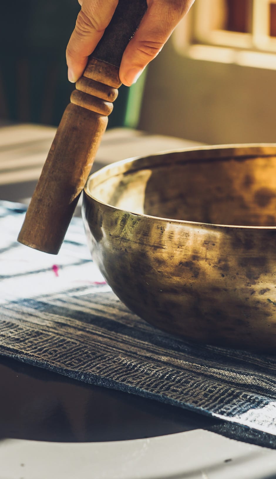 A hand using a stick to hit a sound bowl