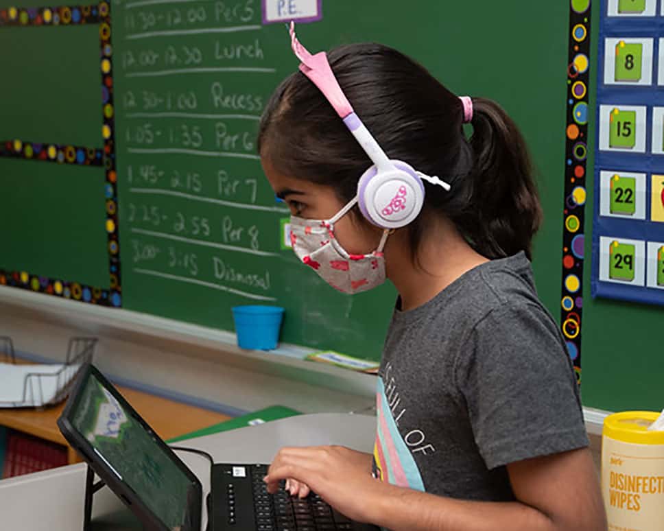 A student in a masking working on an assignment on her computer.